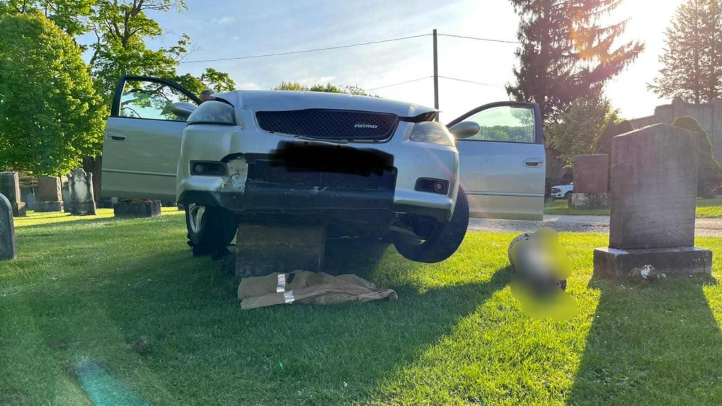 A car rests on top of a headstone at the Greenwood Cemetery after crashing through the Owen Sound, Ont., cemetery on Tues., May 24, 2022 (Owen Sound Police/Twitter)